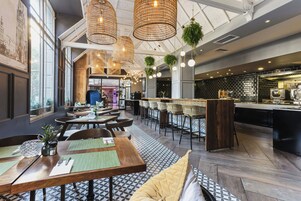 A restaurant interior with high ceilings, hanging wicker light fixtures, and a bar area with stools.