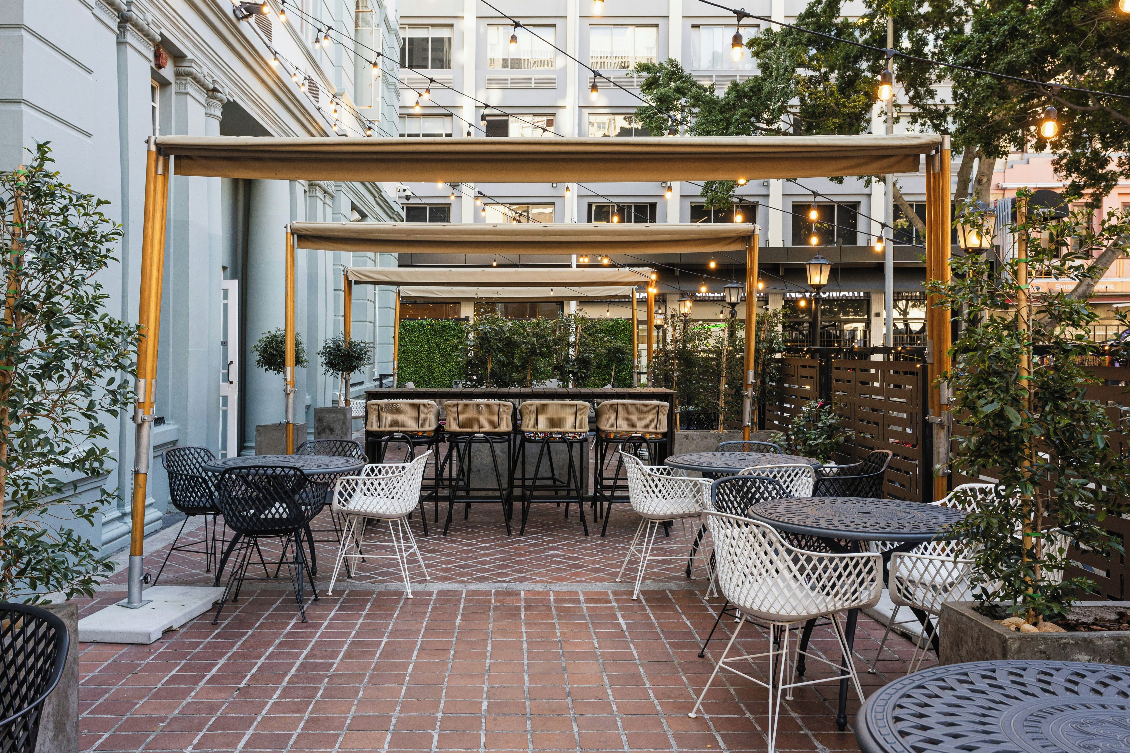 An outdoor patio with tables and chairs, a pergola, and a brick floor.
