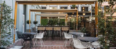 An outdoor patio with tables and chairs, a pergola, and a brick floor.