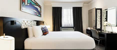 A hotel room with a large bed, a desk, a chair, a desk lamp, a wall-mounted TV, and a window with curtains.