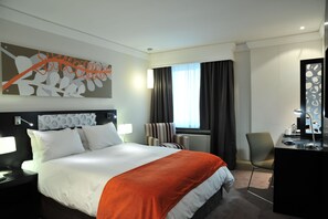 Relax in a stylish room with a large bed, desk, and comfortable armchair, offering a view of the outside.
