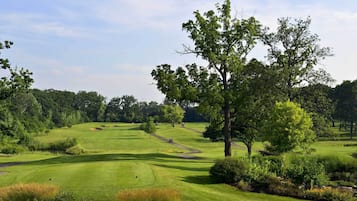 A golf course with well-maintained grass, trees, and a clear sky.