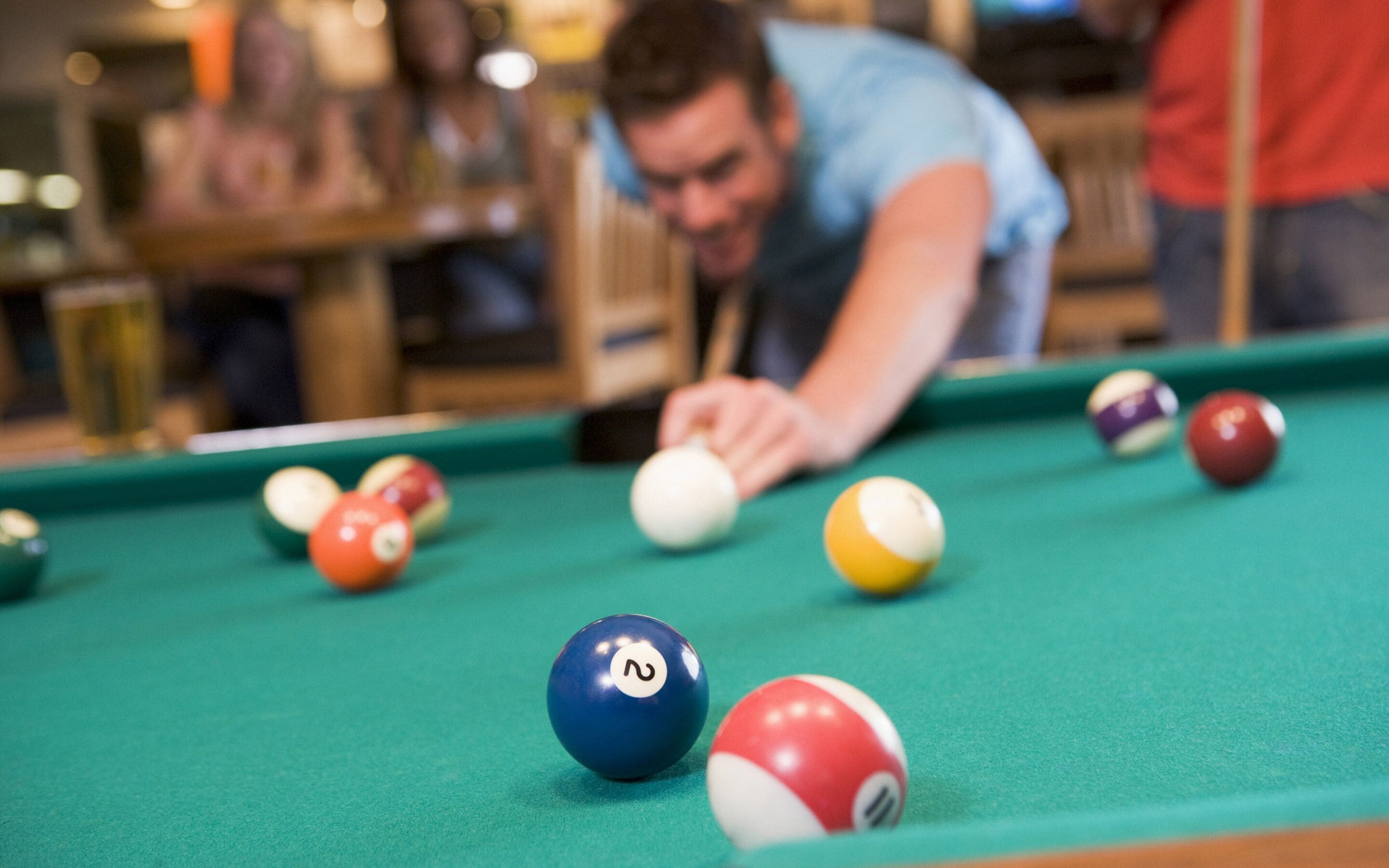A pool table with balls and a person leaning over it.