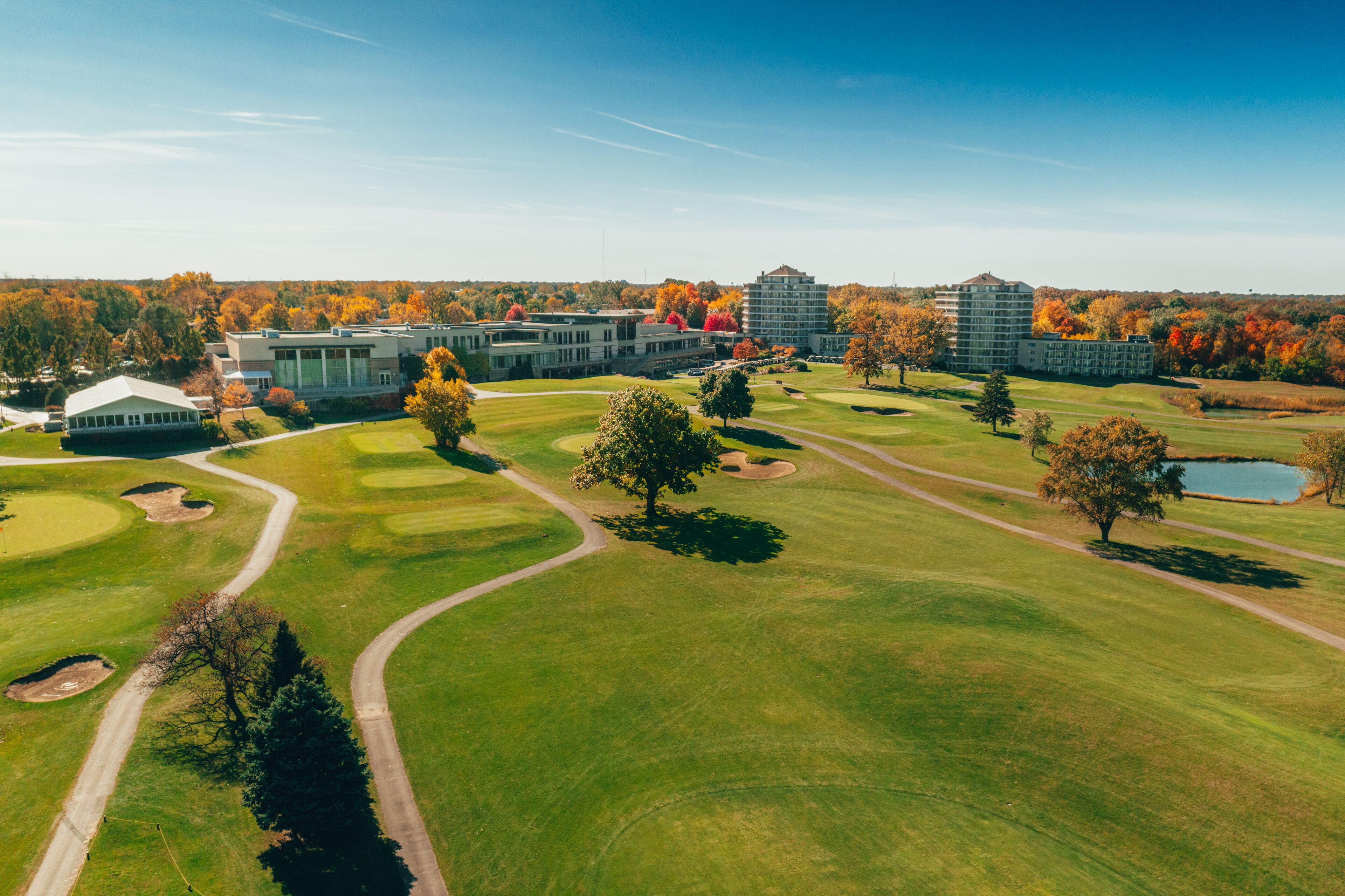 An aerial view of a golf course with multiple buildings, including a large hotel with a modern design and a smaller building with a traditional roof.