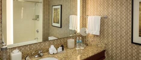Un baño de hotel con lavamanos de encimera de granito, un espejo grande y una zona de ducha.