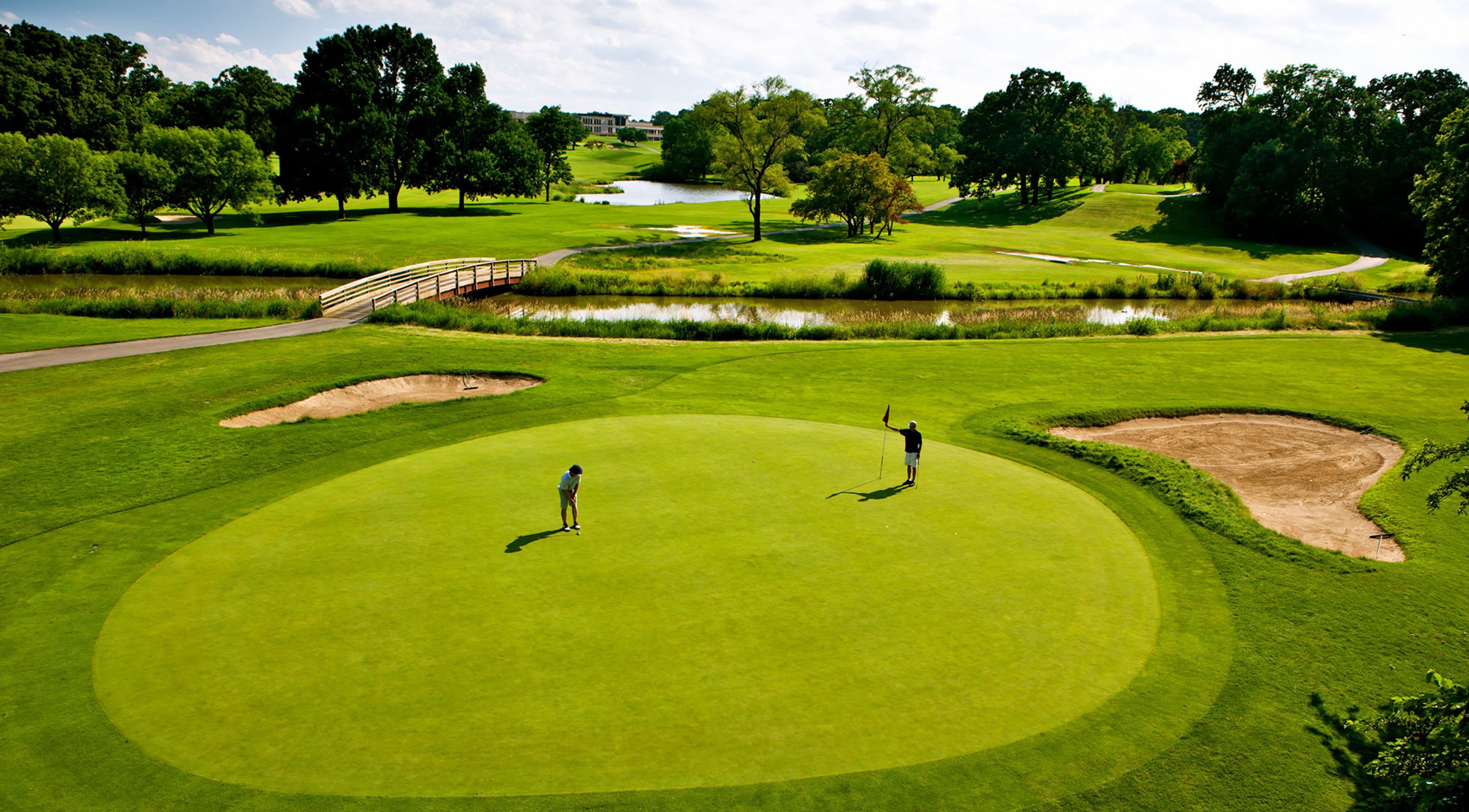 Ein Golfplatz mit Teich, Sandbunkern und einer Brücke.