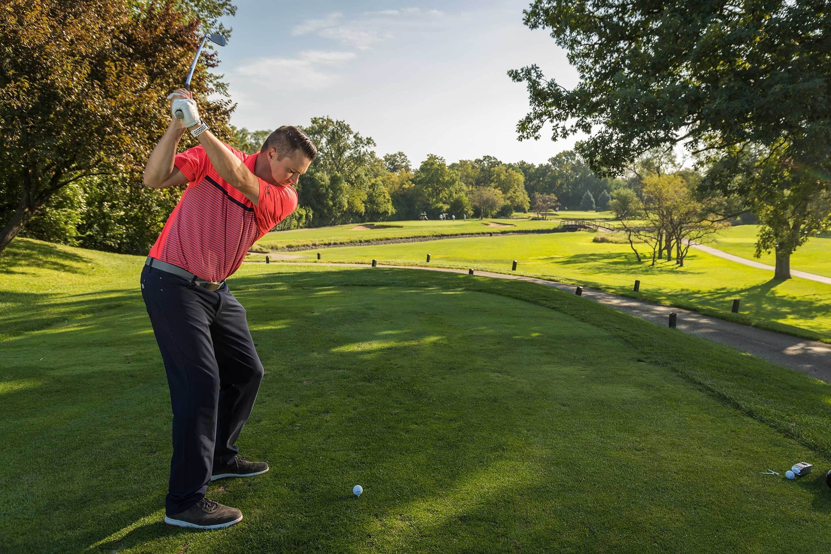 A golf course with a well-maintained green, a clear sky, and a path running alongside the course.