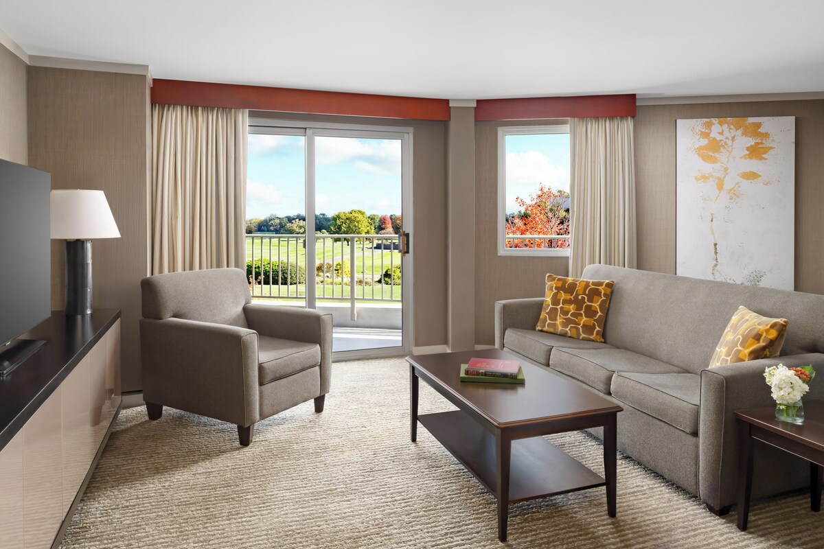 A modern hotel room with a sofa, armchair, and a flat-screen TV.