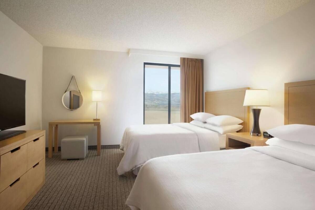 Une chambre d’hôtel avec deux lits, un bureau, une télévision et une grande fenêtre donnant sur un beau paysage.