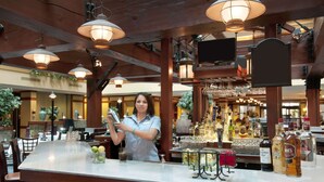 Eine Bar mit einem Barkeeper, der Getränke zubereitet, Holzbalkendecke und einer Auswahl an Flaschen und Gläsern auf der Theke.
