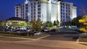 Ein mehrstöckiges Hotel mit einem gut sichtbaren „Embassy Suites“-Schild, einem Parkplatz mit mehreren Autos und einer gepflegten Grünfläche.