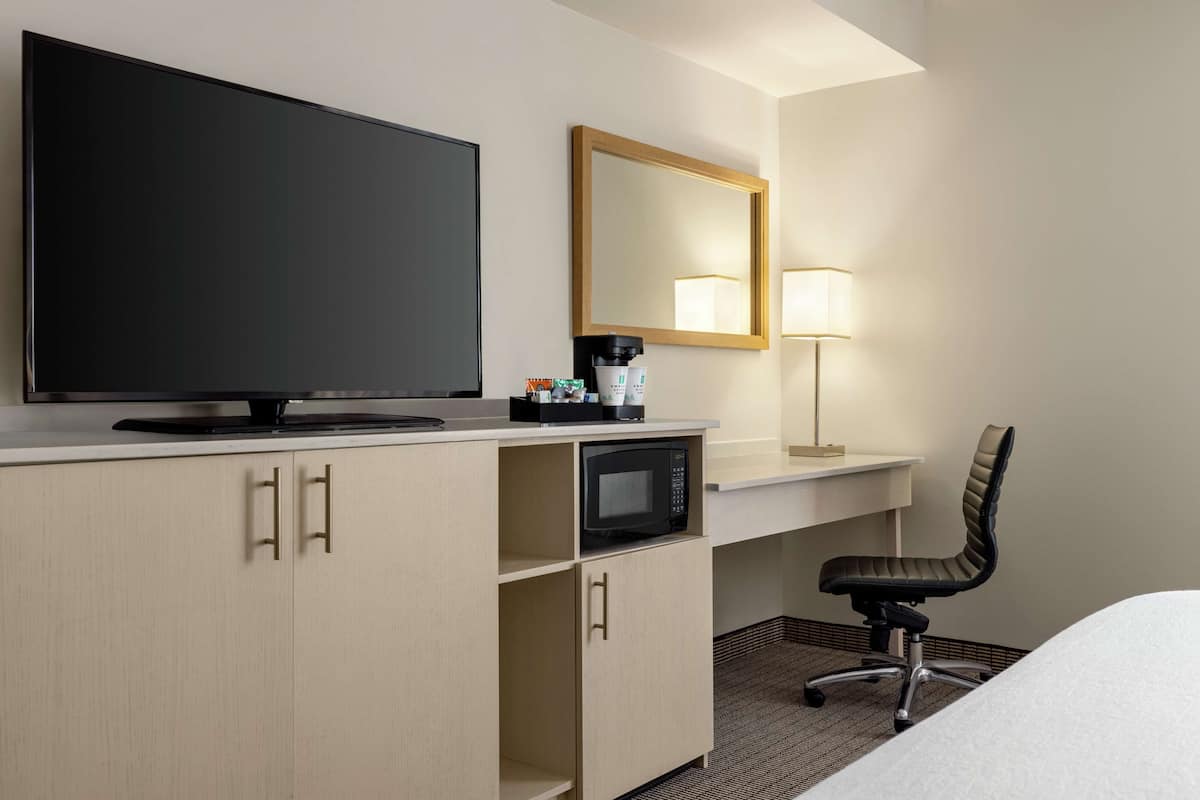 Une chambre d’hôtel équipée d’une télévision à écran plat, d’un four à micro-ondes, d’un bureau avec une lampe et d’une chaise.
