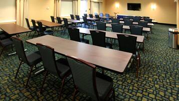 A conference room with multiple tables and chairs, a projector screen, and a television on the wall.