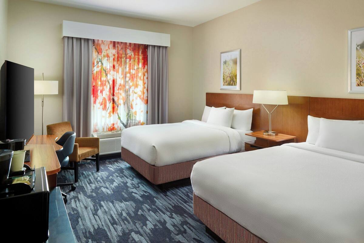 A hotel room with two beds, a desk, a chair, a TV, and a window with curtains.
