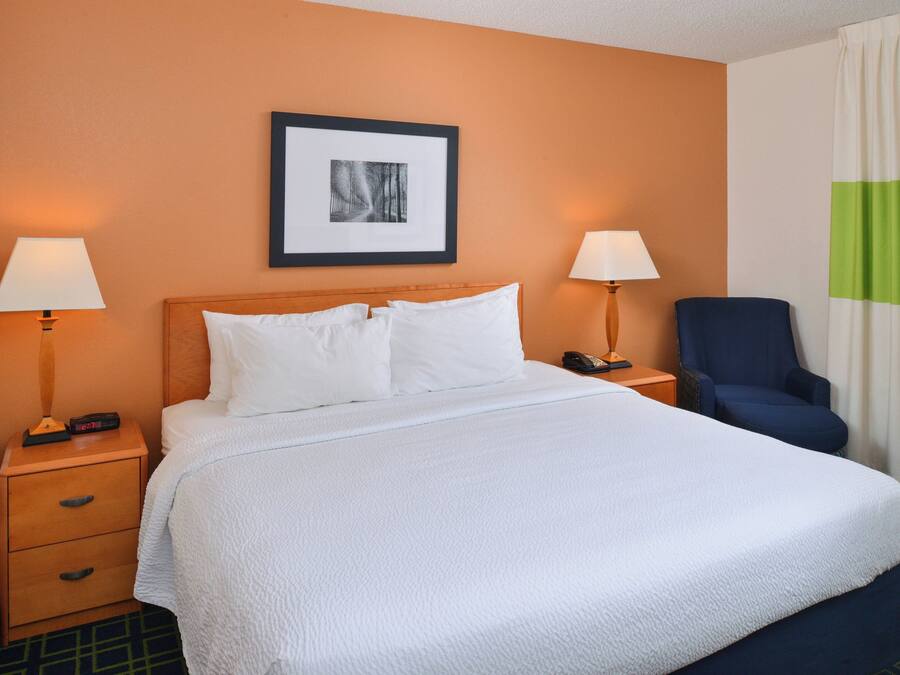 A neatly made bed with white linens, two bedside tables with lamps, a framed picture on the wall, and a blue chair.