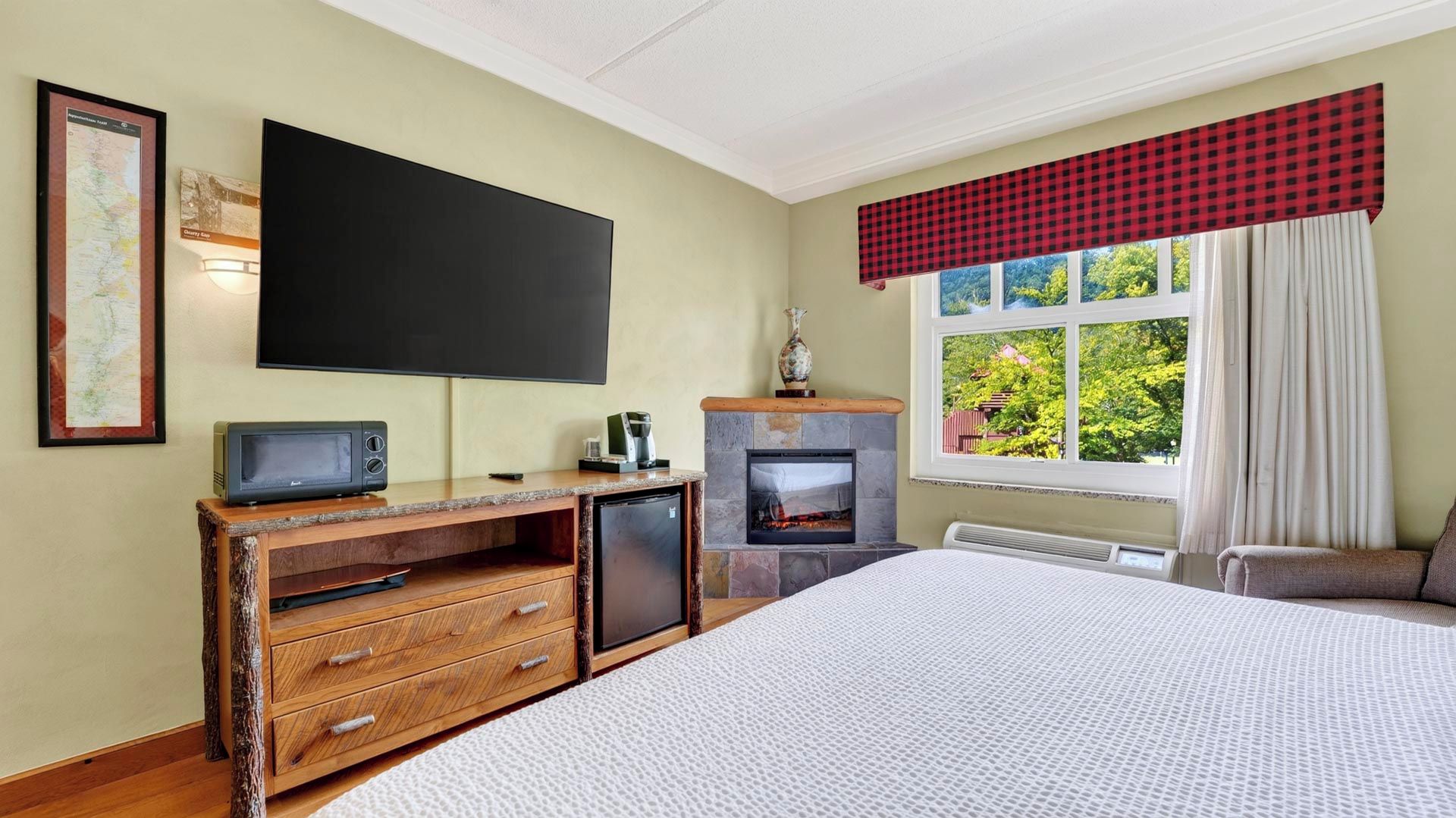 A bedroom with a bed, a television, a fireplace, a desk with drawers, and a window with curtains.