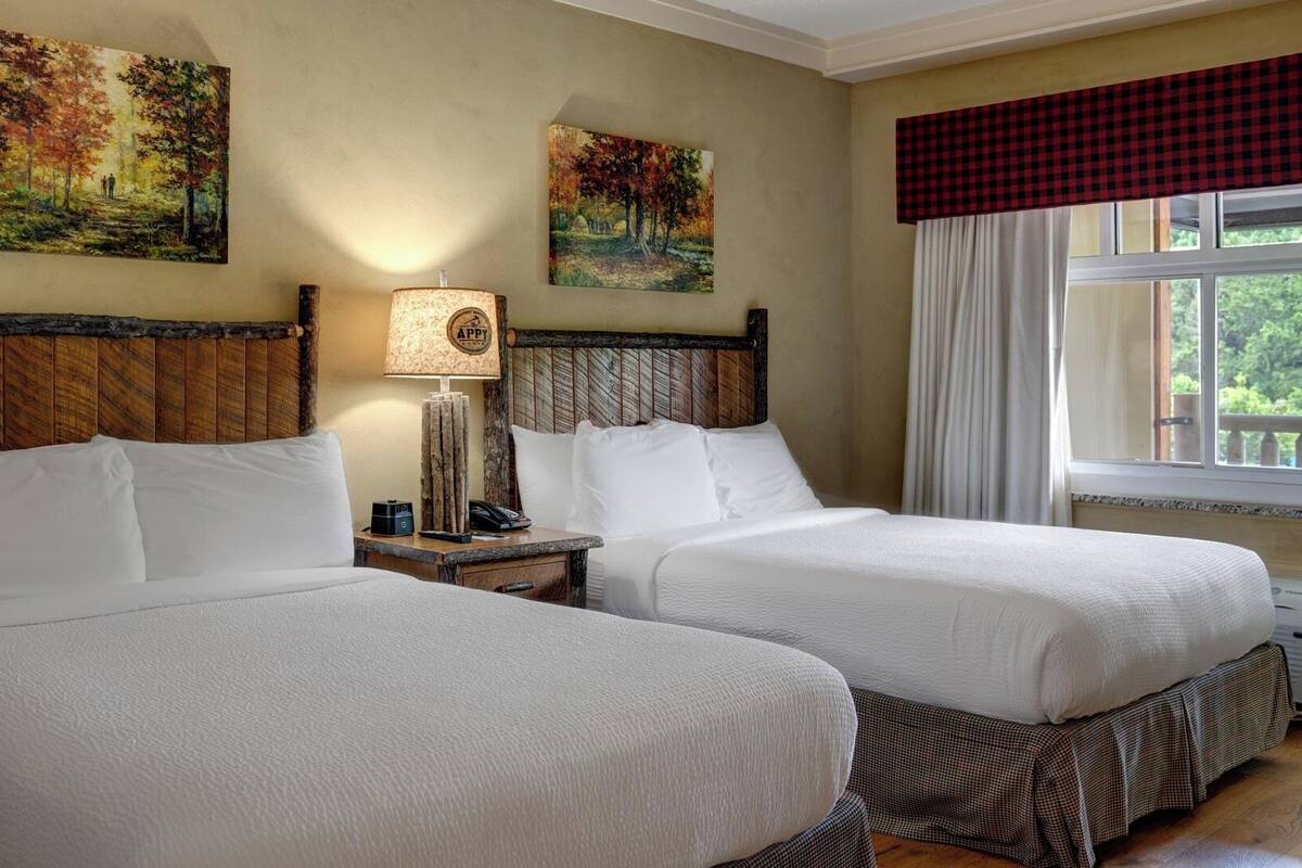 A hotel room with two beds, wooden headboards, and paintings of autumn landscapes.