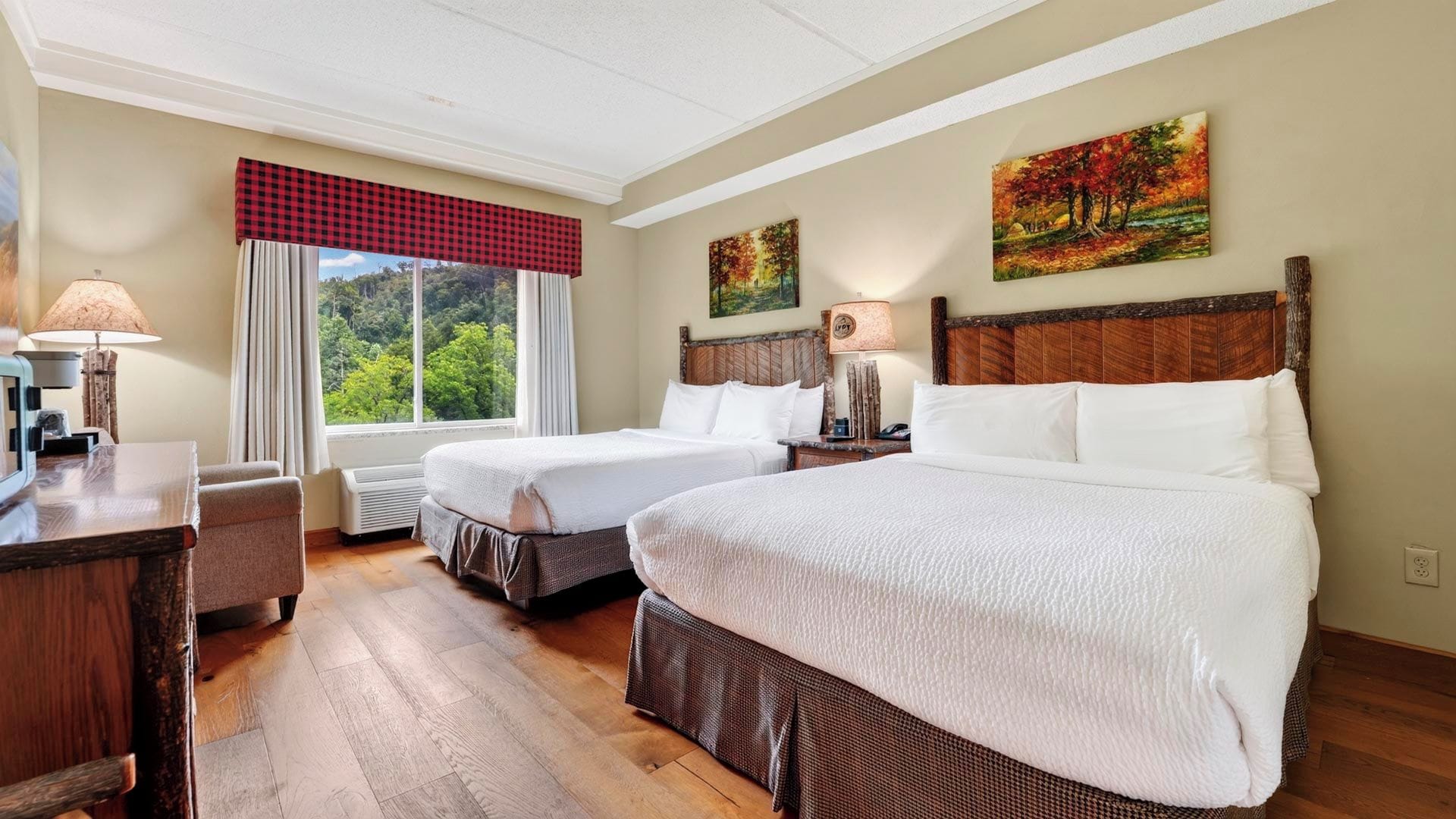 Habitación de hotel con dos camas, un escritorio y una ventana con vistas a árboles.