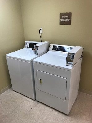 Two stacked front-loading washers in a corner with a wall-mounted sign indicating cycle times.