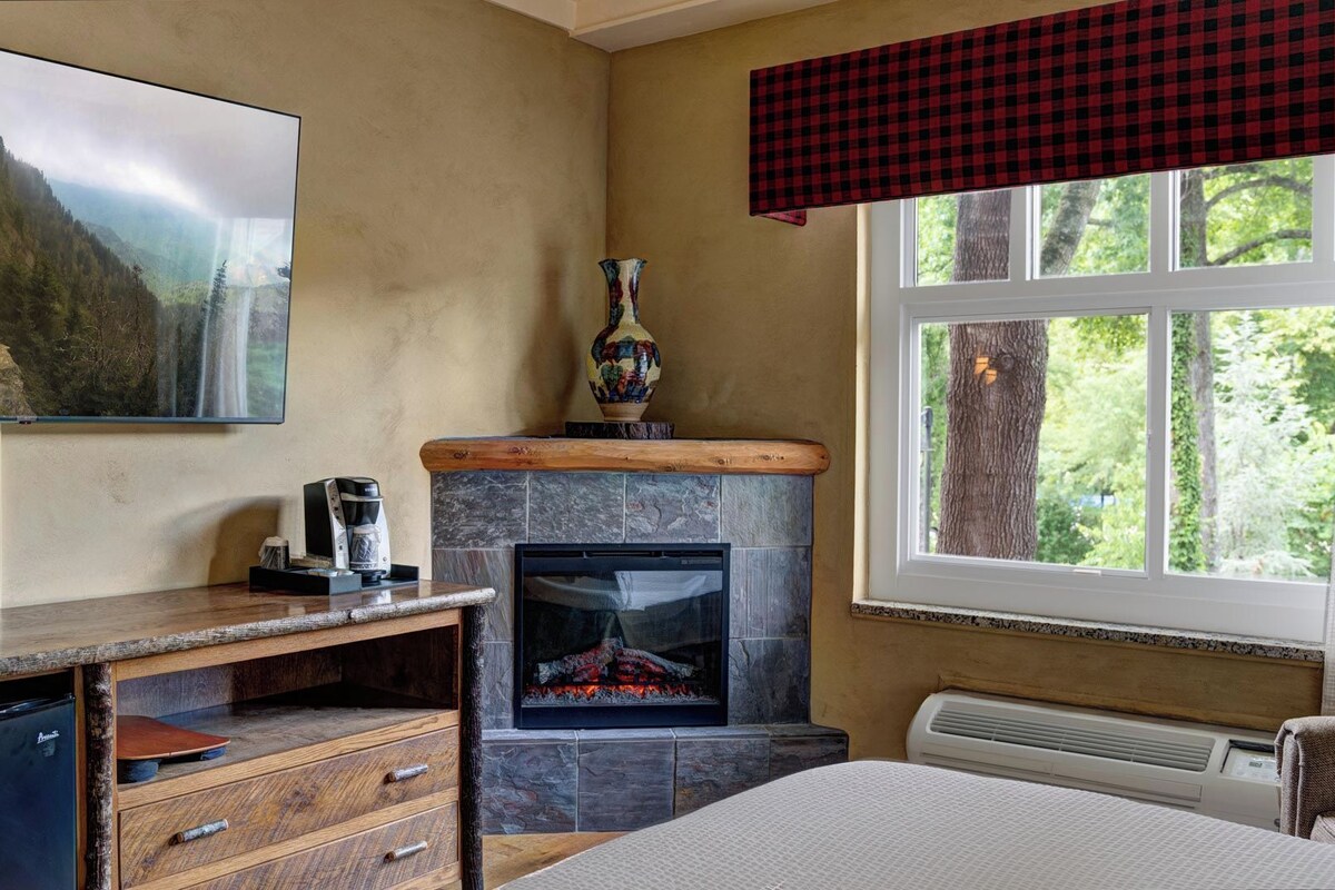 Una habitación acogedora con chimenea, un televisor montado en la pared y una ventana con vistas a árboles.