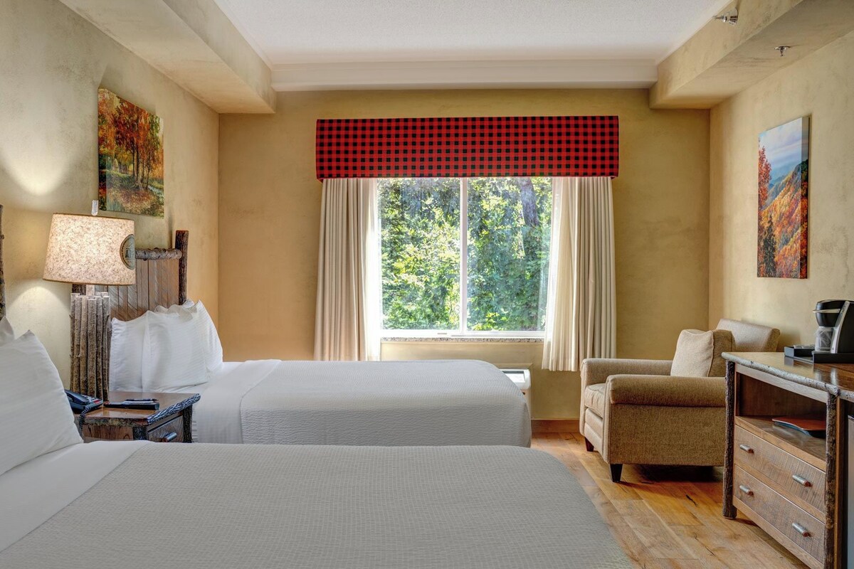 Una habitación de hotel con dos camas, un escritorio con silla, una lámpara y obras de arte en las paredes.