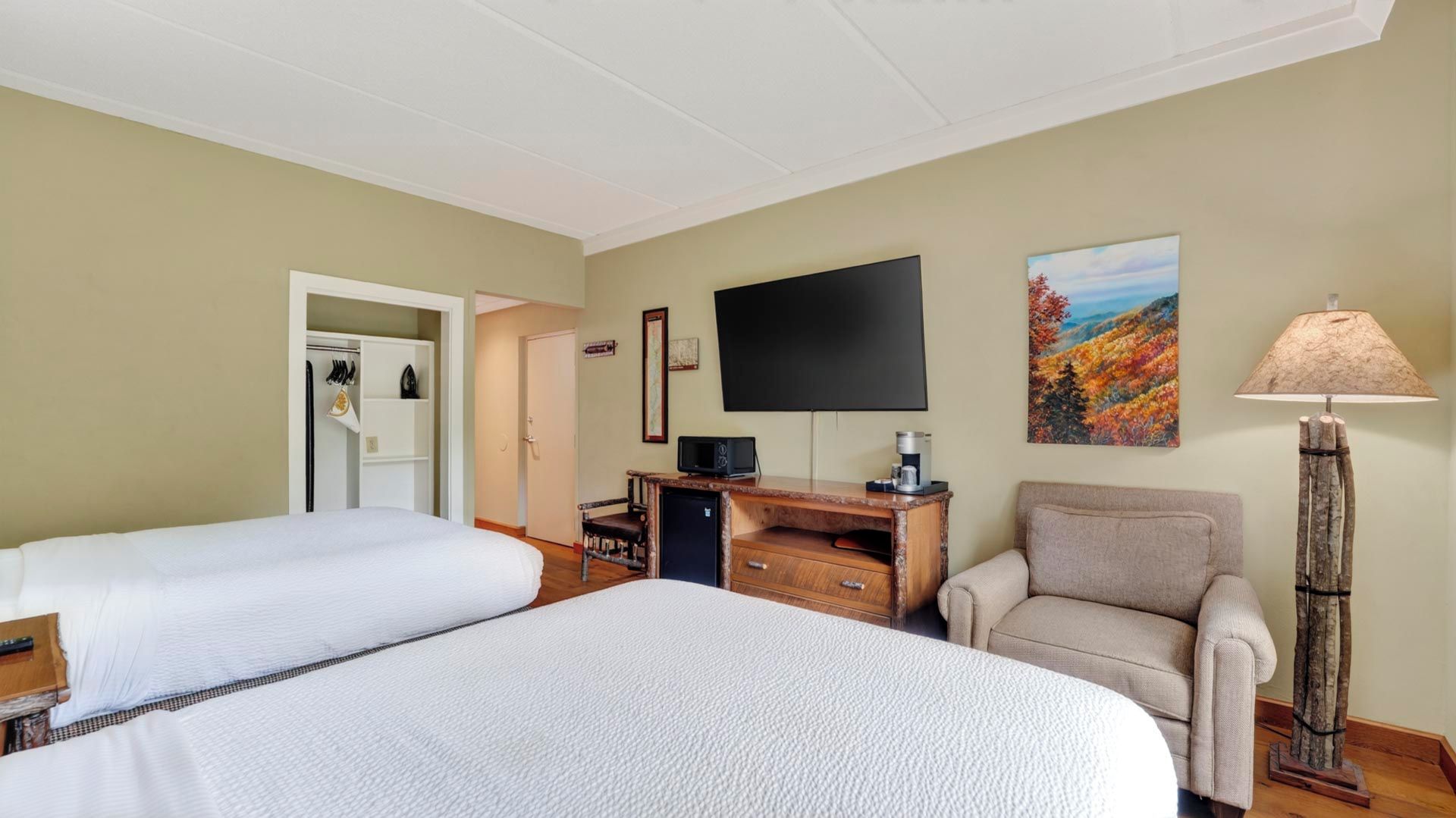 A hotel room with two beds, a desk with a television, a chair, and a lamp.