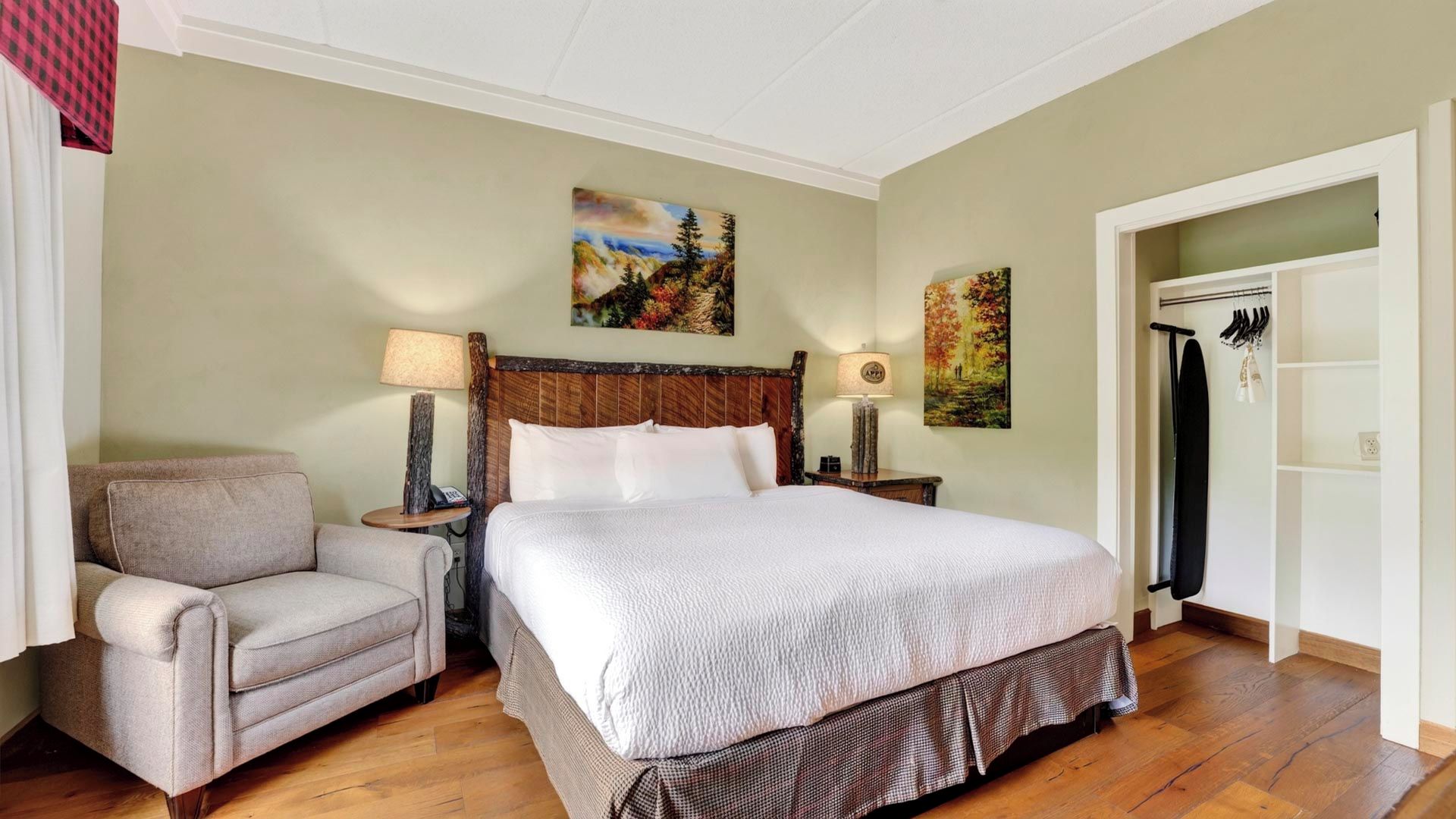 Une chambre d’hôtel avec un lit, une chaise, une armoire et deux tableaux accrochés au mur.