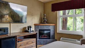 Une pièce chaleureuse avec une cheminée, un téléviseur fixé au mur et une fenêtre donnant sur les arbres.