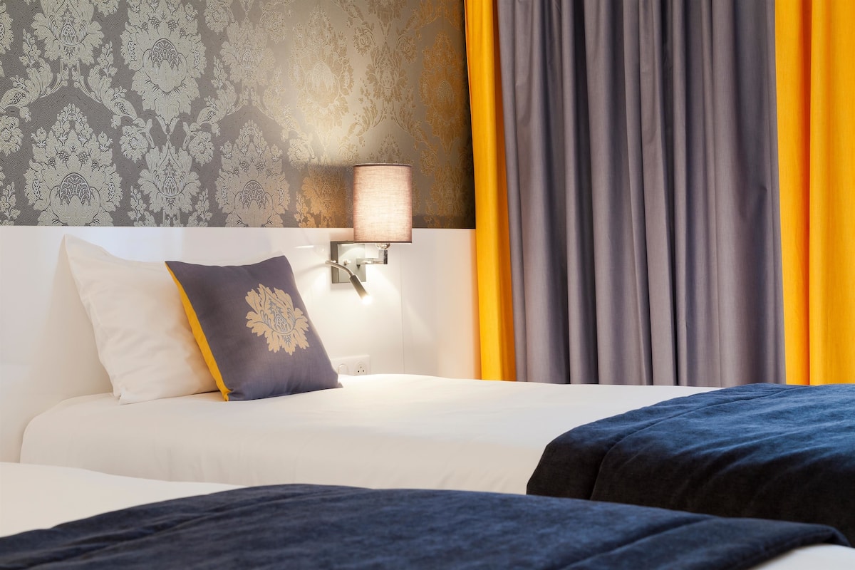 Una habitación de hotel con una cama, una mesita de noche con lámpara y una ventana con cortinas.