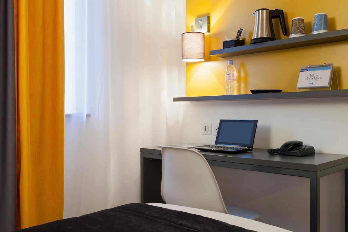 Habitación de hotel con escritorio, computadora portátil, teléfono y estantes con artículos de aseo y un calendario.