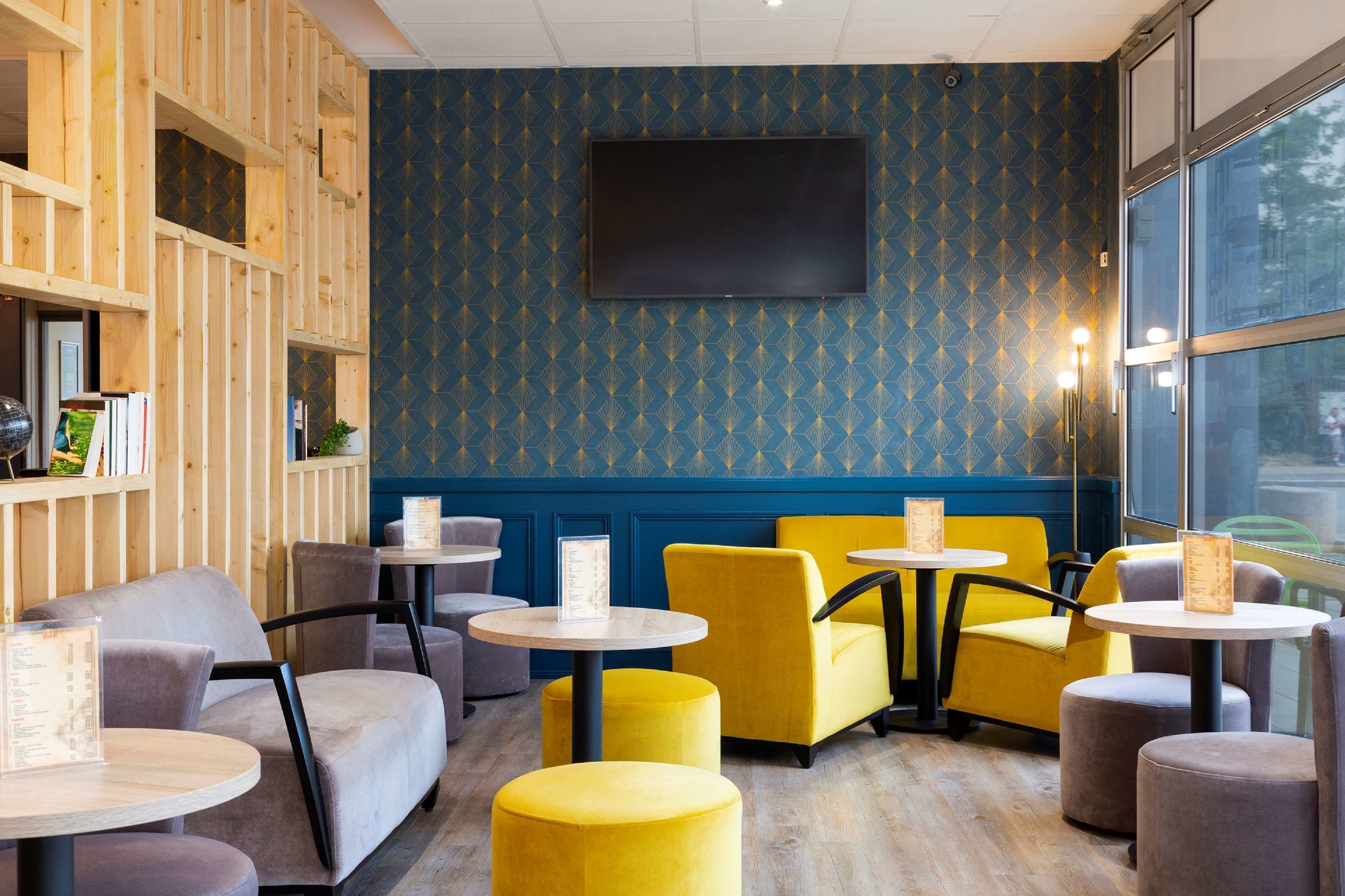 A cozy seating area with round tables and chairs, a large flat-screen TV mounted on the wall, and a patterned blue wall.