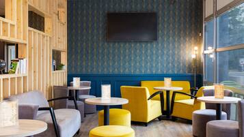 A cozy seating area with round tables and chairs, a large flat-screen TV mounted on the wall, and a patterned blue wall.