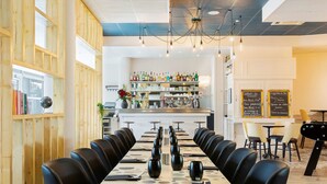 Un restaurante con una larga mesa de comedor, sillas negras y una zona de bar al fondo.