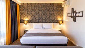 Une chambre d’hôtel avec un grand lit, deux lampes de chevet, un climatiseur fixé au mur et un élément décoratif mural.
