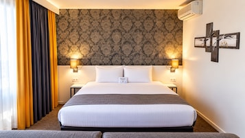 Une chambre d’hôtel avec un grand lit, deux lampes de chevet, un climatiseur fixé au mur et un élément décoratif mural.