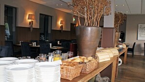A buffet setup with plates, baskets, and a large vase with dried branches. - Fletcher Hotel De Geulvallei (Valkenburg aan de Geul)