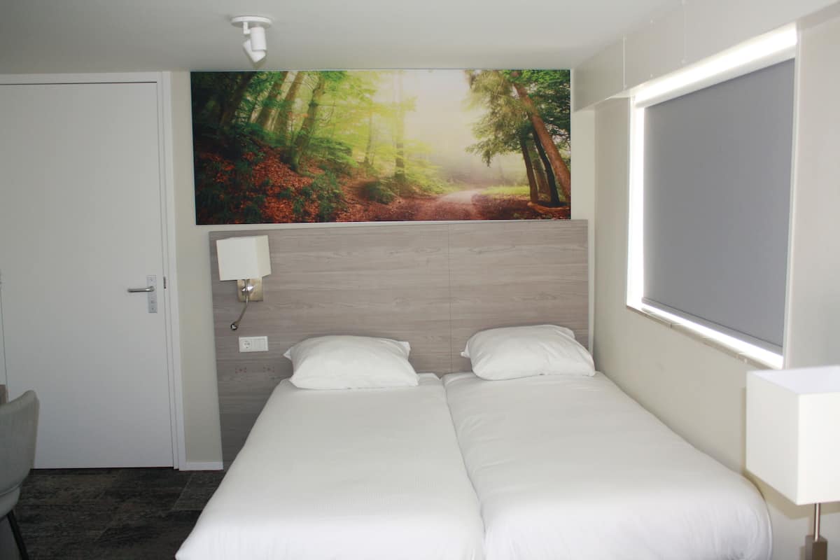 A hotel room with a bed, a desk, and a large forest-themed painting on the wall.