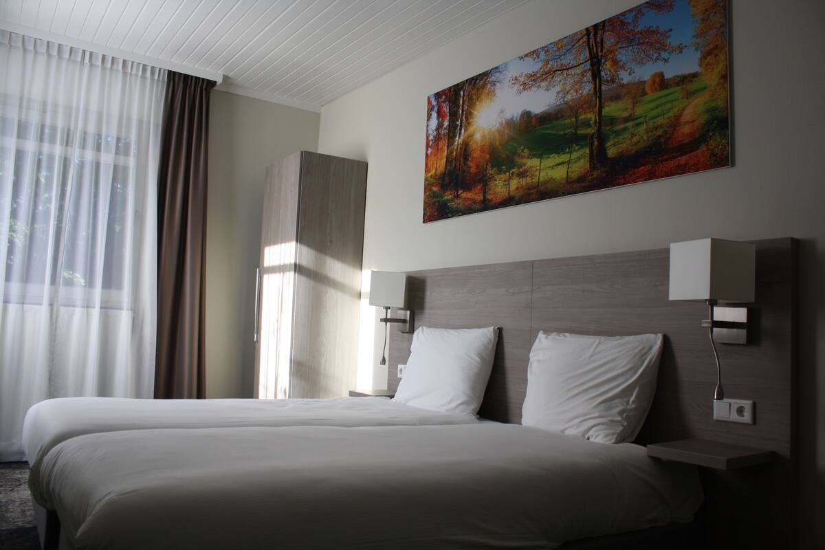 A hotel room with a large bed, two bedside tables, a nightstand, and a painting on the wall.