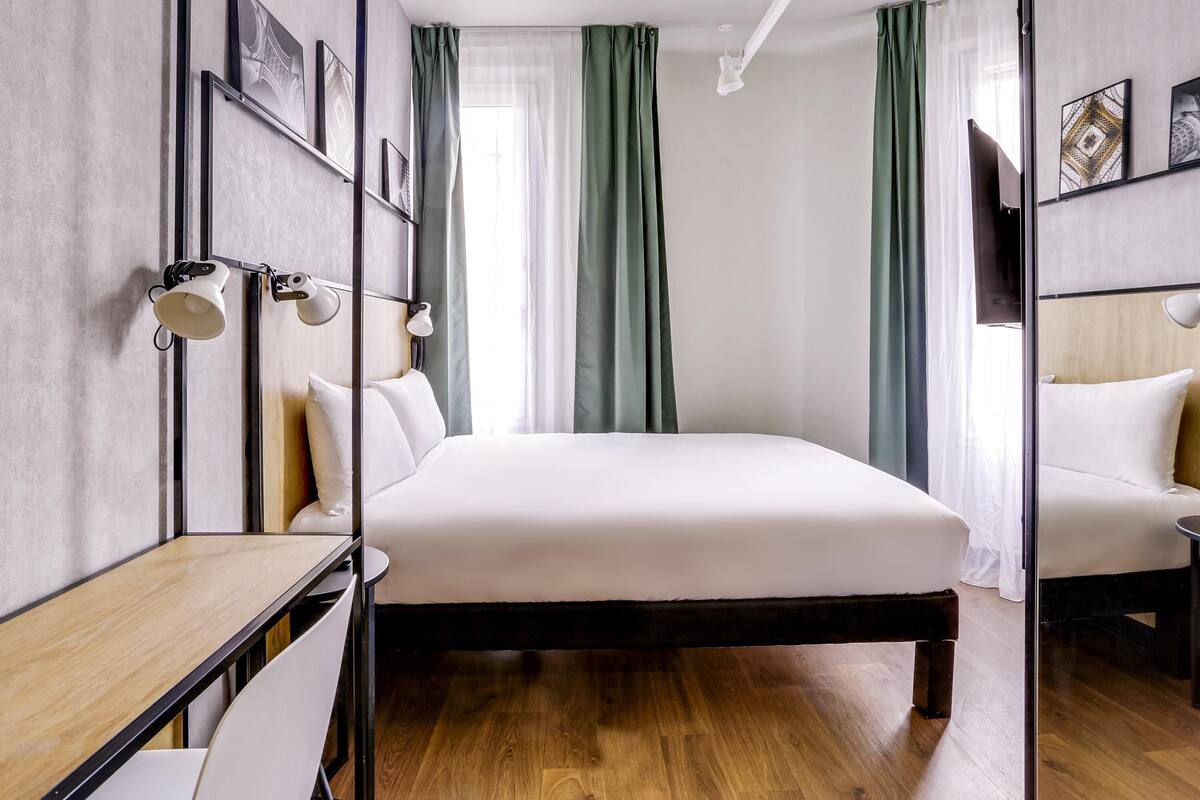 A modern hotel room with a large bed, a desk, and a TV.