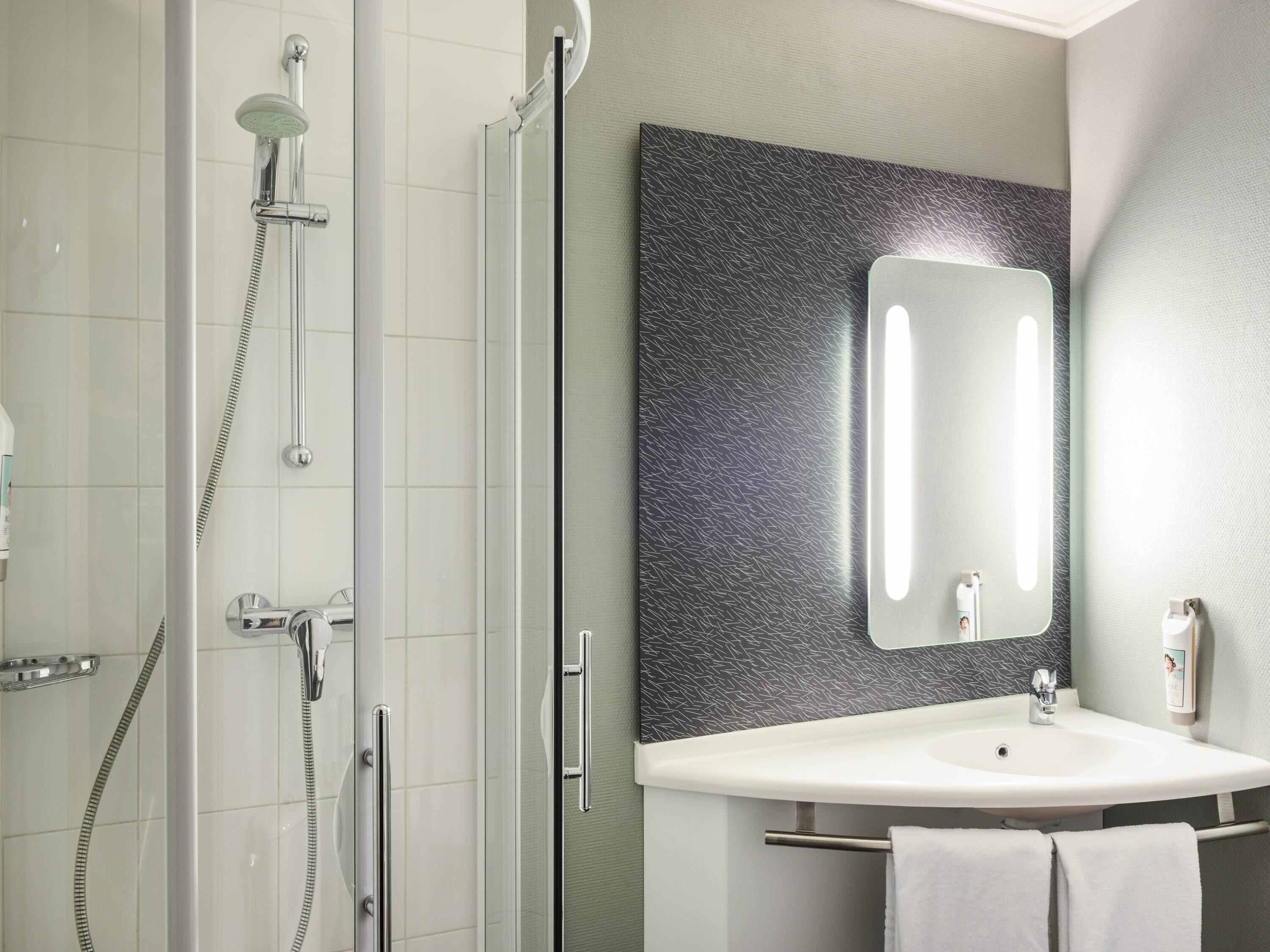 Een moderne badkamer met een douchecabine van glas, een wit wastafelmeubel en een grote spiegel met een gestructureerde achterwand.