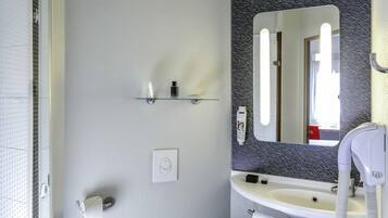 Un baño con un lavamanos blanco, un espejo con un respaldas negro estampado, un secador de pelo y una toalla colgada en la pared.