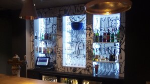 A bar area with a patterned wall, shelves with bottles, and a cash register. - ibis Orange Sud (Orange)