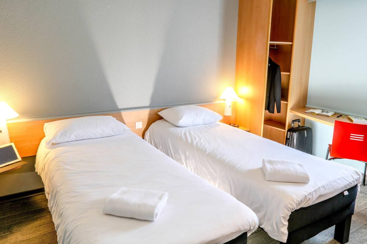 Una habitación de hotel con dos camas, un escritorio, una silla, un armario y una lámpara.