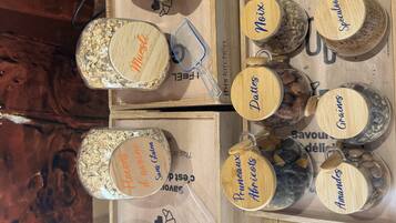 A wooden display with various food items labeled with names like "Corn Flakes," "Muesli," and "Pruneaux Abricots."