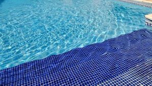 A swimming pool with clear blue water, surrounded by a building with a tiled roof and a balcony. - ibis Orange Sud (Orange)