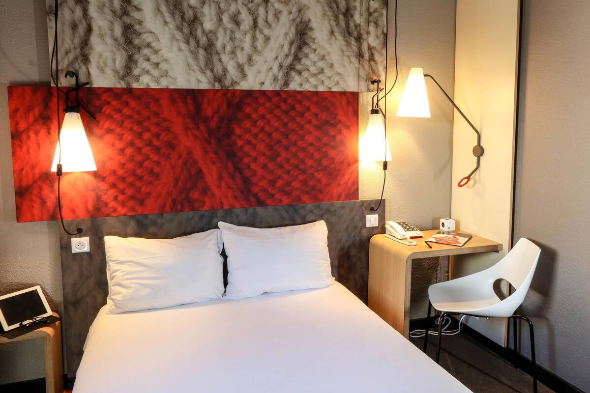 Una habitación de hotel con cama, mesita de noche, silla, escritorio y una gran obra de arte en la pared.