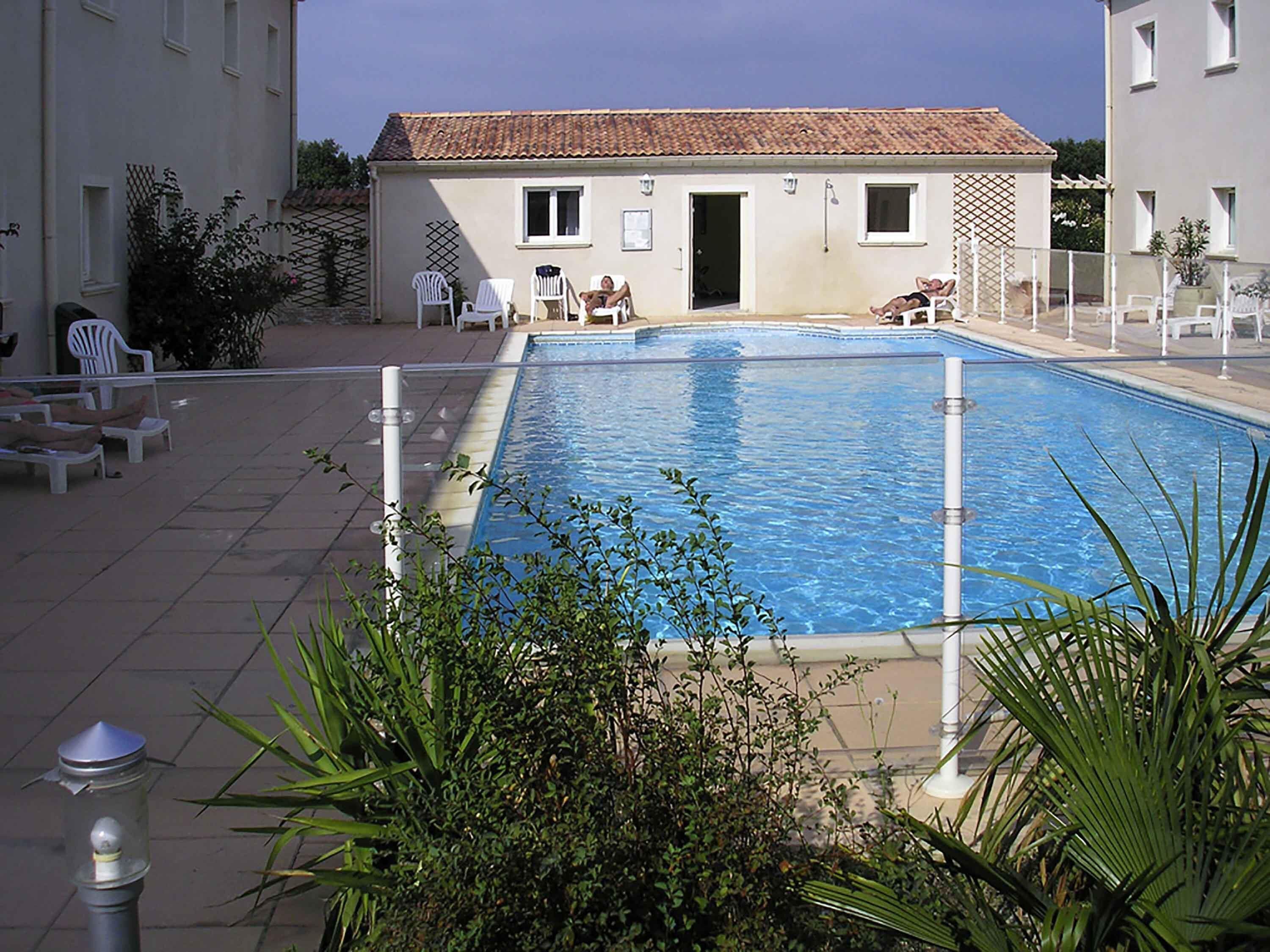 A swimming pool with lounge chairs and a building with a tiled roof.