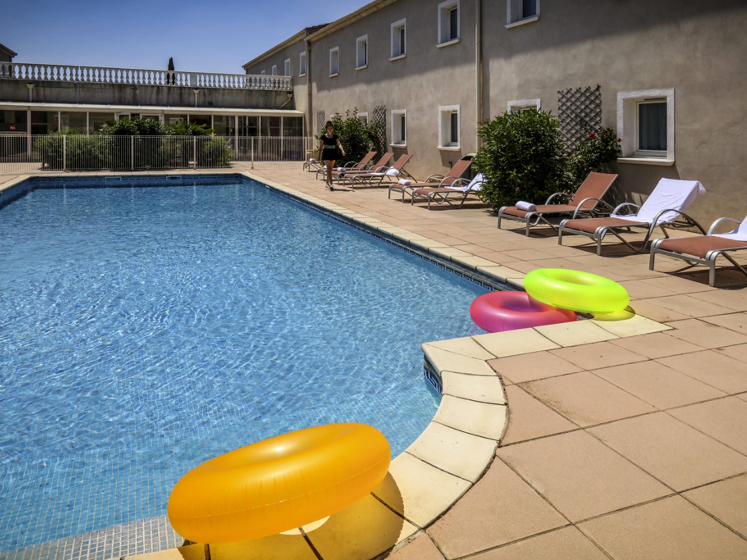 A swimming pool with lounge chairs and inflatable rings.