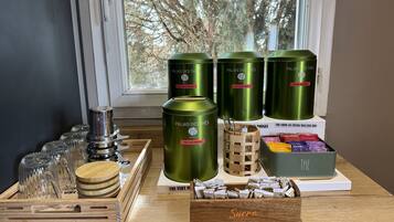 Une exposition de récipients cylindriques verts portant l’étiquette « Palais des Thés », avec divers noms de thés, un plateau en bois contenant de la verrerie et une boîte étiquetée « Sucre ».