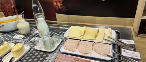 Une table de buffet proposant divers aliments, notamment du fromage, du jambon et une bouteille de lait.